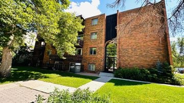 Calgary apartment for rent - A red brick building with a black roof and a tree in front of it.
