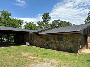 Newalla house for rent - A stone building with a black roof and a brown garage door.