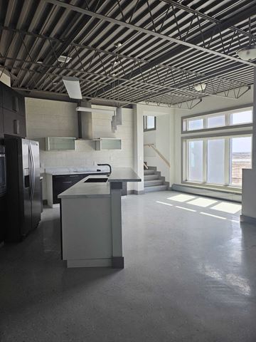 Estevan apartment for rent - A large, empty room with a kitchen area and a staircase.