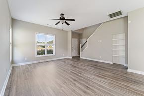 Jacksonville house for rent - A spacious room with a ceiling fan and light, hardwood flooring, and a staircase leading to another level.