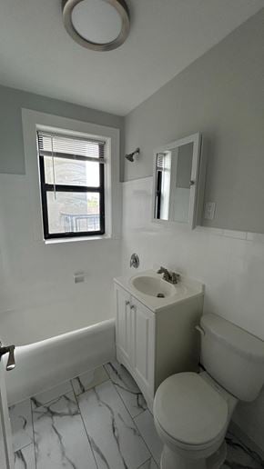 Bergenfield apartment for rent - A white toilet sits in a bathroom with a marble floor and a window.