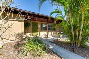 Sarasota house for rent - the front of a yellow house with palm trees and a sidewalk