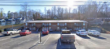 Gray apartment for rent - a parking lot with cars in front of a brick building