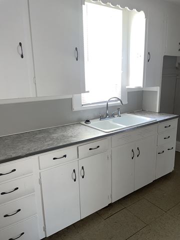 Lima apartment for rent - A kitchen with white cabinets and a sink under a window.