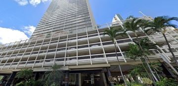 Honolulu apartment for rent - A tall building with a palm tree in front of it.