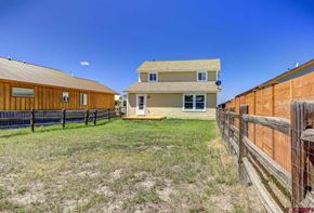 Pagosa Springs house for rent - A wooden fence surrounds a grassy yard with a two-story house in the background.