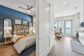 Tampa apartment for rent - A bedroom with a bed and a ceiling fan, and a kitchen with a refrigerator and a sink.