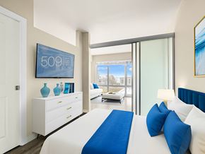 Seattle apartment for rent - Staged bedroom with a plush bed, dresser, and a view through to the living area at 509 1st in Seattle.