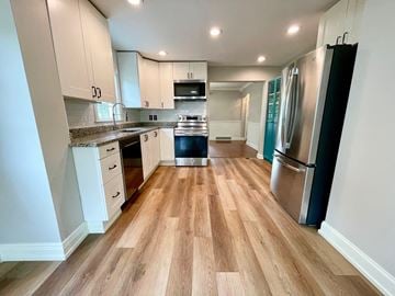 Louisville house for rent - a kitchen with wood floors and white cabinets and stainless steel appliances