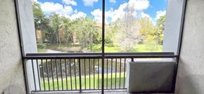 Plantation apartment for rent - A balcony with a black railing and a window overlooking a green lawn and trees.