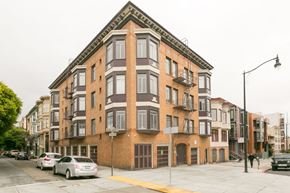 San Francisco apartment for rent - A street view of a multi-story building with cars parked in front.