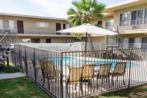 Tustin apartment for rent - A pool surrounded by a black fence with chairs and an umbrella.