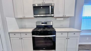 Angleton house for rent - a kitchen with white cabinets and a stove and a microwave