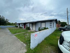 Vero Beach apartment for rent - A white car is parked in front of a grey building with a red door.