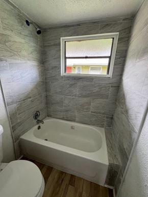 Palmetto apartment for rent - A white toilet sits next to a bathtub in a bathroom with grey tiles.