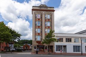 New Britain apartment for rent - A tall building with a red and white facade stands in front of a white building and trees.