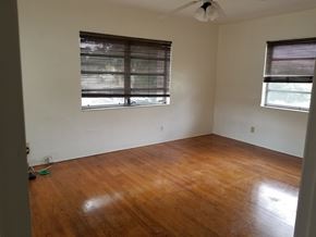 Hallandale apartment for rent - A room with wooden floors and two windows with blinds.