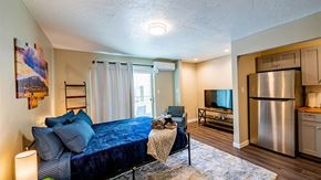 Albuquerque apartment for rent - A bedroom with a blue bedspread and a stainless steel refrigerator in the kitchen area.