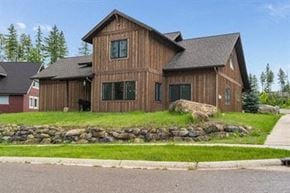 Whitefish house for rent - a brown house with a grass yard and a stone wall