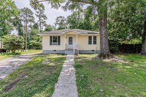 Jacksonville house for rent - A small house with a grey door is surrounded by greenery.