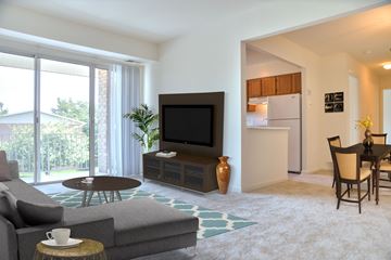 Frederick apartment for rent - A living room with a grey couch, a brown coffee table, a flat screen TV, a dining table with chairs, and a kitchen in the background.