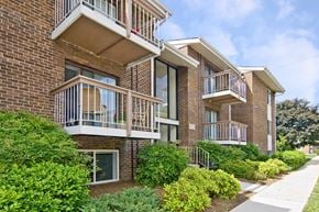 Glen Burnie apartment for rent - A brick apartment building with balconies and bushes in front.