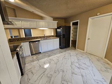 Houston house for rent - a kitchen with marble flooring and white cabinets and a black refrigerator