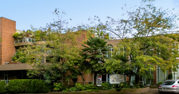 Vancouver apartment for rent - A building with a sign that says "The Cottage" is surrounded by trees and bushes.