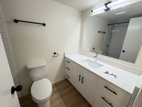 Victoria apartment for rent - A white toilet is in a small bathroom with a sink and mirror.