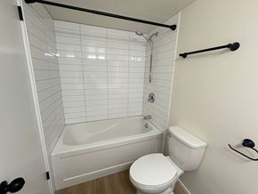 Victoria apartment for rent - A white toilet sits next to a white bathtub in a bathroom with white tiles.
