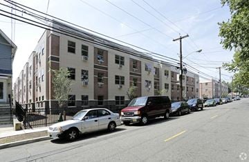 Newark apartment for rent - A street view of a residential area with cars parked on the side of the road and apartment buildings in the background.