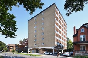 Ottawa apartment for rent - A tall building with a brown facade stands in front of a red brick house.