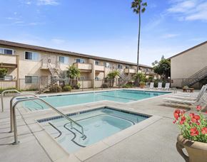 Anaheim apartment for rent - A pool surrounded by chairs and a building in the background.