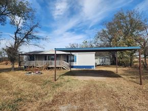 Shawnee house for rent - A house with a blue roof and white walls is surrounded by dry grass and trees.