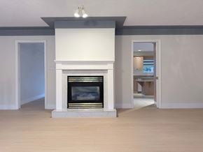 Victoria apartment for rent - A white fireplace with a black screen is in the middle of a room with light wood flooring.
