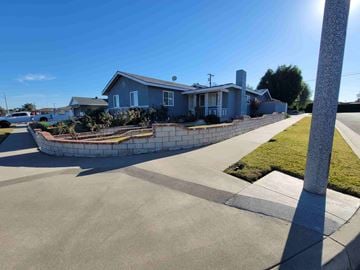 Whittier house for rent - A house with a blue roof and a white fence is surrounded by a grassy area and a concrete walkway.