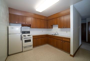 Regina apartment for rent - A kitchen with a white refrigerator and stove, brown cabinets, and a white counter.