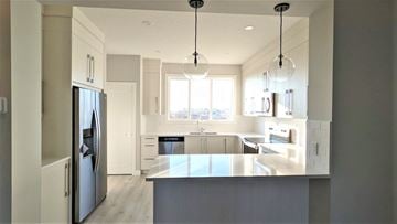 Chestemere house for rent - A modern kitchen with a refrigerator on the left and a countertop with a sink.
