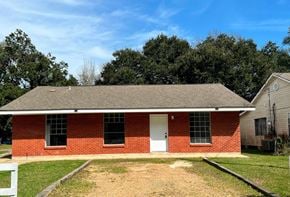 Gulfport house for rent - A red brick house with a white door and a white fence.