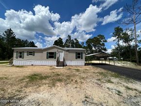Interlachen house for rent - A house with a grey roof and white walls is surrounded by a grassy area with a few trees.