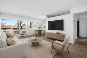 Regina apartment for rent - A living room with a white couch, a wooden coffee table, and a large flat-screen TV mounted on the wall.