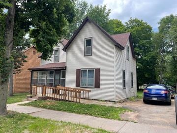 Menomonie house for rent - a white house with a porch and a blue car parked outside