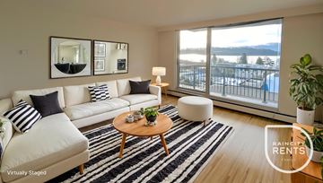 West Vancouver apartment for rent - A living room with a white couch, a coffee table, and a large window overlooking a snowy landscape.