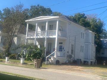 Mobile house for rent - A white two-story house with a porch and a tree in front.
