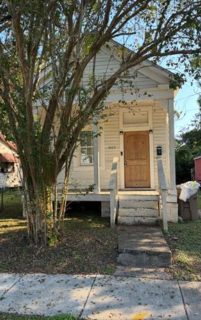 Mobile house for rent - A small white house with a brown door and a tree in front.
