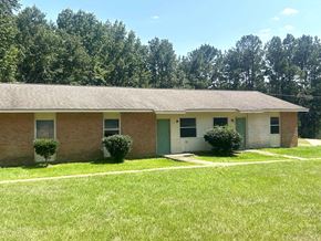 Gloster apartment for rent - a brick house with a grassy yard and trees in the background