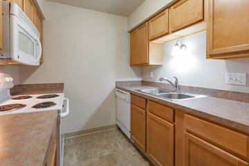 Dewitt apartment for rent - A kitchen with a white stove top oven, a white dishwasher, and wooden cabinets.