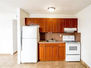 Davie apartment for rent - A white refrigerator stands next to a kitchen with brown cabinets.