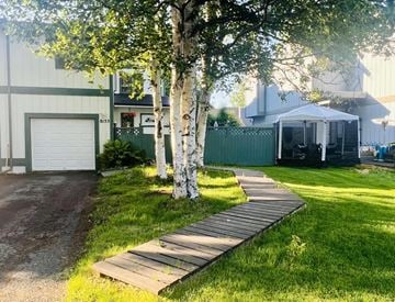Anchorage house for rent - a backyard with a wooden pathway and trees in front of a house
