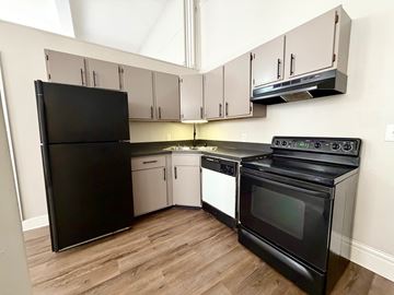 Louisville apartment for rent - A black refrigerator and oven in a kitchen with wooden floors and white cabinets.